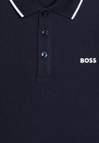 Polo shirt bleu marine en tissu texturé, avec un col classique, trois boutons et un logo "BOSS" blanc sur le côté gauche.