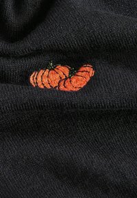Tessuto a maglia nero con fantasie di zucche arancioni ricamate, che mostra un design testurizzato con fili morbidi e una sottile profondità nei punti di cucitura.