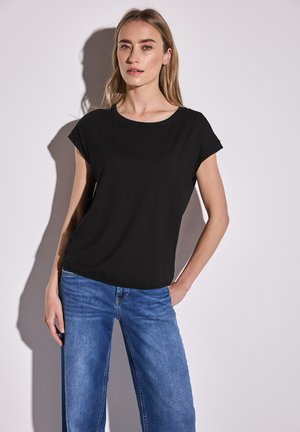 Zwarte top met korte mouwen en een ronde halslijn, gemaakt van een zachte stof. Gecombineerd met lichtblauwe wijde jeans. Eenvoudig ontwerp.