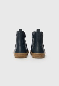 Botas de tobillo de cuero azul marino con un acabado suave, suela de goma marrón, lengüetas para tirar y cremalleras laterales para un fácil calzado.