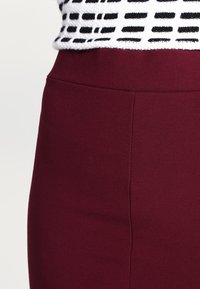 Bordeauxfärgad figurnära kjol i slät tyg med ren sömdetalj, kombinerad med en texturerad topp i svart och vitt mönster.