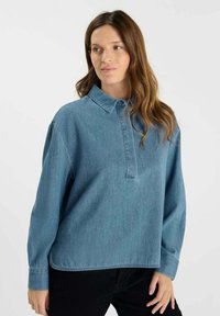 Lichtblauw denim overhemd met een kraag, lange mouwen en een halve knoopsluiting; zichtbare textuur en subtiele details door het hele shirt.