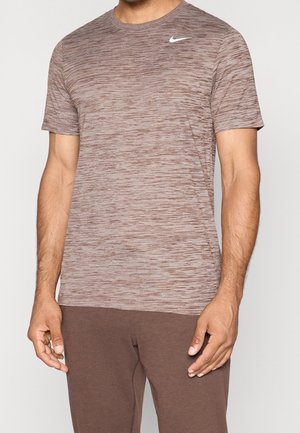 Mand iført en brun, meleret Nike sportst-shirt med korte ærmer og et hvidt swoosh-logo på brystet.