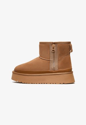 Bruine suède enkellaarzen met een zijrits, ronde neus en een dikke zool. Gelaagd afwerking met een gladde accent rond de zoolrand.