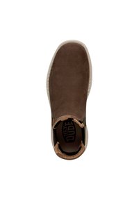 Zapato marrón tipo mocasín con una superficie texturizada suave, acentos elásticos en los laterales y una suela de color claro en contraste. El interior presenta el logo de la marca.