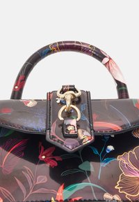 Handväska med blommönster och glansig yta, med svart bakgrund, rundat handtag och detaljer i guld.