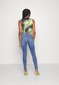 Ärmlös topp med grön och svart gradientmönster samt sidostygn, kombinerad med åtsittande blåjeans och gröna klacksandaler.