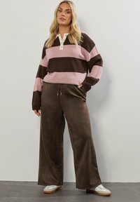 Wzorzysty sweter w kolorze mauve i brązowym z kołnierzykiem i guzikami, zestawiony z szerokimi brązowymi spodniami. Teksturowana tkanina i luźny krój.