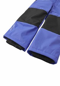 Pantaloni impermeabili blu e neri con cinturini elastici e una texture liscia. Presentano un bloccaggio di colore prominente e un dettaglio con zip all'orlo.