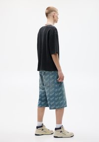 Sort ribbet kortærmet skjorte med afslappet pasform; lyseblå denimshorts med gentagen logo mønster; creme sneakers med mørke detaljer.