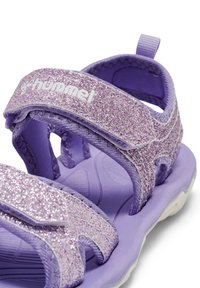 Lila sandaler med glittriga remmar, textil- och gummimaterial, kardborreknäppningar och en dämpad sula.