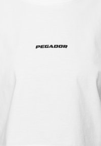 Hvidt stof med sort tekst i store bogstaver "PEGADOR" centreret på brystområdet.