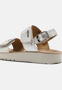 Silverfärgade metallsandaler med justerbara remmar, texturerad ovandel och en beige plattformssula. Har ett spänne för säker passform.