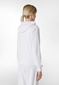 Weißer Kapuzenpullover aus weichem, strukturiertem Stoff. Mit gerippten Bündchen und lockerer Passform. Sichtbare Nähte und eine Kängurutasche.