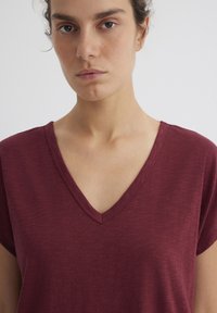 Maroon V-neck t-shirt with short sleeves, featuring a soft texture and a subtle heather pattern. The collar has a stitched edge detailing.