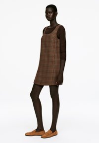 Braun kariertes Kleid mit quadratischem Ausschnitt, kurzer Silhouette und glatter Textur. Kombiniert mit hellbraunen Wildleder-Lederwaren.