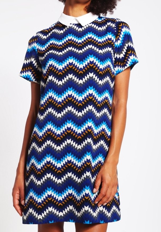 Vestido de manga corta con un collar blanco. Presenta un patrón en zigzag en azul, marino y marrón. Hecho de una tela suave, diseño hasta la rodilla.