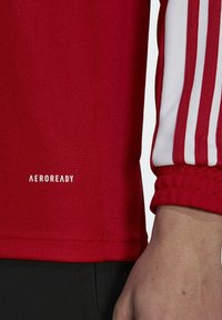Red athletic shirt with white three-stripe accents on sleeves. Features smooth texture and "AEROREADY" logo in white.