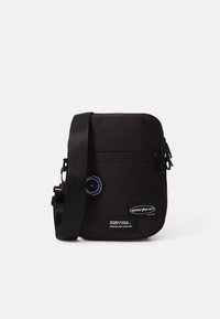 Black crossbody bag with a smooth texture, rectangular shape, adjustable strap, blue circular detail, and branded patch on the front.