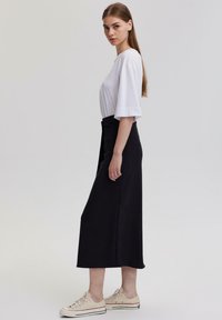 Bílý zkrácený tričko s volnými rukávy, spárované s černou midi sukní a béžovými teniskami, s elegantním, minimalistickým designem.