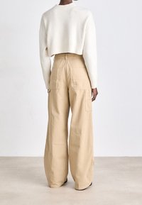 Cream cropped sweater with ribbed trim, paired with wide-leg beige cargo pants featuring side pockets and a smooth texture.