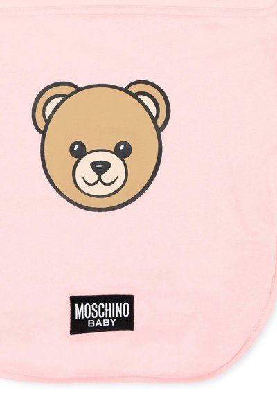 Jasnoróżowy śliniaczek dla niemowląt z uśmiechniętą twarzą misia oraz czarną metką "Moschino Baby" na dole, na środku.