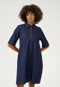 Denim shirtjurk in donkerblauw met korte mouwen, kraag, een vijfknops sluiting en zichtbare contrasterende stiksels. Voorzien van steekzakken.