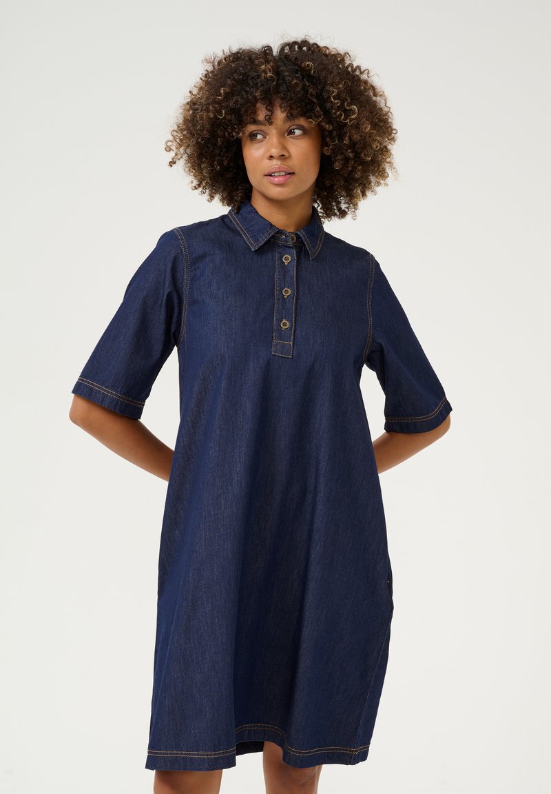Denim shirtjurk in donkerblauw met korte mouwen, kraag, een vijfknops sluiting en zichtbare contrasterende stiksels. Voorzien van steekzakken.
