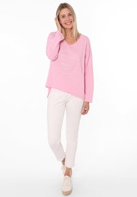 Rosa Langarmtop aus strukturiertem Stoff mit rundem Logo-Print. Kombiniert mit weißen, figurbetonten Hosen und beigen Espadrilles im Sneakers-Stil.