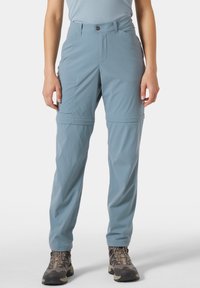 Vaaleansiniset retkeilyhousut, joissa on kevyestä kankaasta valmistetut vetoketjulliset lahkeet, sivutaskut, nappisuljin ja väljähkö istuvuus.