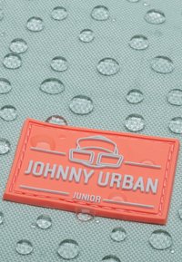 Fényes narancssárga műanyag logó címke, az "JOHNNY URBAN JUNIOR" dombornyomott felirattal, textúrázott, vízálló menta zöld háttérrel, cseppekkel.