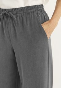 Grijze joggerbroek gemaakt van zachte stof, met een elastische tailleband met een trekkoord en zijzakken voor extra gemak.