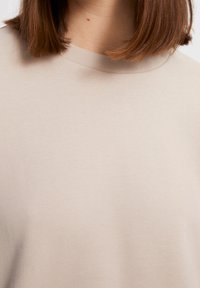 Maglione color beige chiaro con un collo a costine morbido. Il tessuto appare soffice con una sottile texture e senza schemi o accenti visibili.