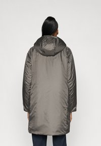 Cappotto imbottito grigio con cappuccio, caratterizzato da una texture leggera e liscia e una silhouette leggermente strutturata. Dettaglio di un unico bottone sulle maniche.