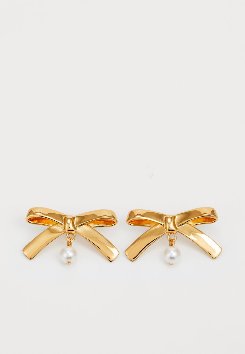 Gold-tone metal earrings shaped like bows, featuring smooth curves and a hanging pearl accent. The design is flat with a shiny finish.