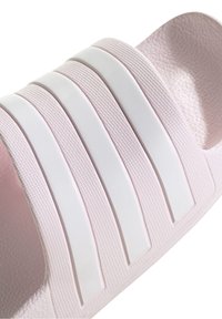 Světle růžové pantofle na klínu s texturovaným svrškem, zdobené třemi bílými vodorovnými pruhy a hladkou vnitřní stranou. Protiskluzová gumová podrážka.