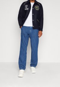 Námořnická bunda z vlněné směsi s bílým lemováním a vyšívanými logy, doplněná světle modrými džínovými kalhotami a bílými teniskami.