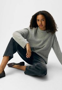 Maglione grigio a maglia con vestibilità rilassata e scollatura a girocollo. Abbinato a pantaloni cropped grigio scuro e ballerine marrone scuro, creando un look casual.