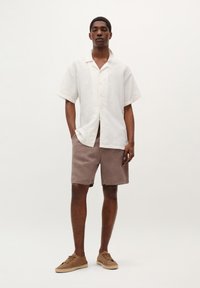 Hvid kortærmet skjorte med knaplukning og en subtil stribet tekstur, parret med brune shorts. Brune casualsko fuldender outfittet.