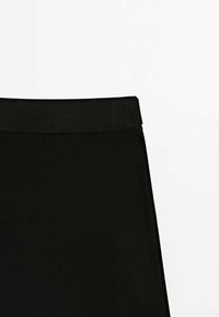 Jupe noire en tissu lisse et extensible. Elle dispose d'une large ceinture plate et d'un design simple et minimaliste ; sans motifs ni embellissements.