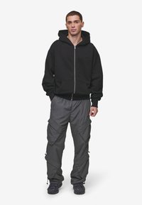 Black zip-up hoodie with a front pocket and ribbed cuffs, paired with gray cargo pants featuring multiple pockets and zippers.