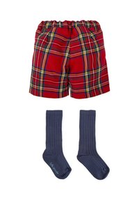 Pantalones cortos a cuadros rojos con cintura elástica y dos bolsillos laterales, combinados con calcetines de canalé oscuras hasta la rodilla.