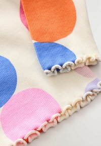 Un tissu côtelé décoré de grandes cercles colorés en bleu, rose, orange et lavande, avec un bord froncé blanc aux extrémités.
