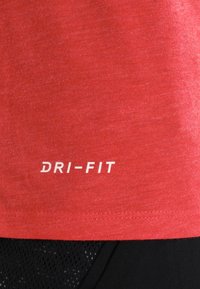 Czerwona koszulka sportowa z białym napisem "DRI-FIT" powyżej czarnych szortów siatkowych.