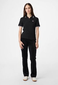 Svart pikétröja med vitrandig krage och muddar, kombinerad med svarta byxor. Pikétröjan har en liten logotyp på bröstet.