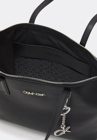 Černá kožená taška tote Calvin Klein se stříbrným zipem, vnitřní kapsou a stříbrným přívěskem "ck" připevněným k rukojeti.