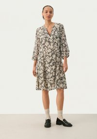 Blumenmuster-Kleid in Beige und Schwarz, knielang, mit V-Ausschnitt und gerafften Ärmeln. Kombiniert mit schwarzen Loafers und beigen Socken.