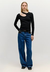 Schwarzes Langarmoberteil mit seitlichem Ausschnitt, kombiniert mit lockeren blauen Denim-Jeans und schwarzen spitzen Knöchelstiefeln.