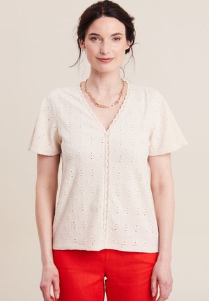 Crème blouse met korte mouwen en een oogjespatroon, V-hals, gegolfde randen en decoratieve stiksel, gecombineerd met rode broek.