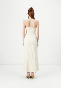 Stroppeløs, tettsittende aftenkjole i off-white med en teksturert stoff. Kjolen faller til midten av leggen, med et flytende design og subtil glans.